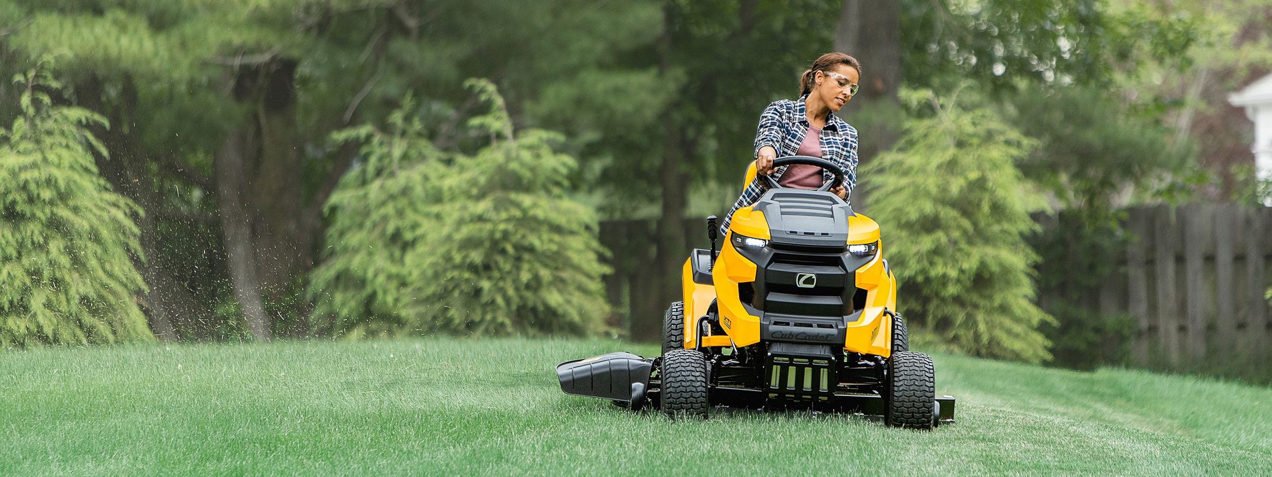 Woman cutting grass on a yellow and black Cub Cadet riding lawn mower